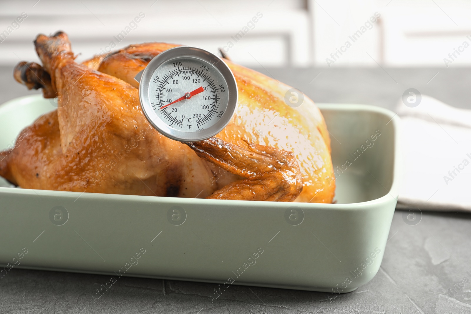 Photo of Roasted turkey with meat thermometer in baking dish on table