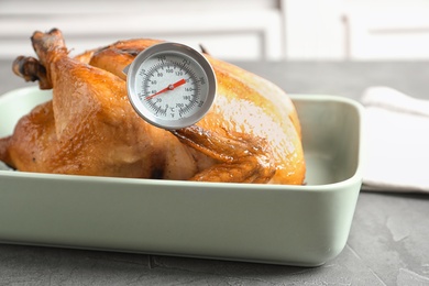 Roasted turkey with meat thermometer in baking dish on table