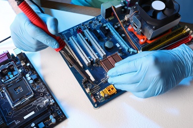 Photo of Technician repairing electronic circuit board with soldering iron at table, closeup
