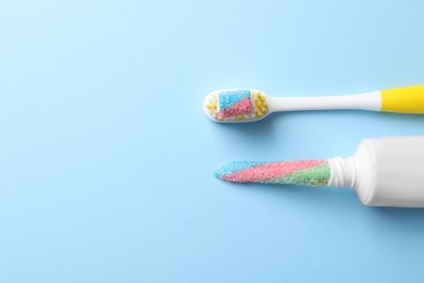 Photo of Toothpaste tube and brush with gummy candies on light blue background, flat lay. Dangers of sugar