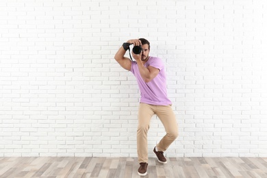 Photo of Young professional photographer taking picture near brick wall. Space for text