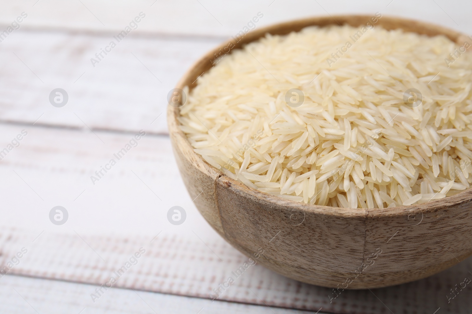 Photo of Raw rice in bowl on light wooden table, closeup. Space for text