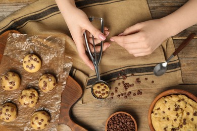 Photo of Woman making delicious chocolate chip cookies at wooden table, top view