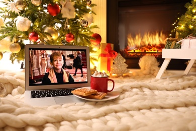 Photo of MYKOLAIV, UKRAINE - DECEMBER 23, 2020: Laptop displaying Home Alone movie near fireplace indoors. Cozy winter holidays atmosphere