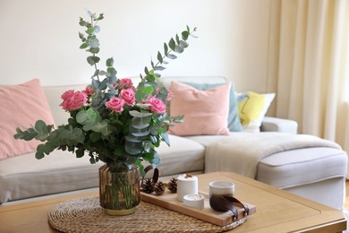 Beautiful bouquet of roses and eucalyptus branches in vase near candles on table at home. Space for text