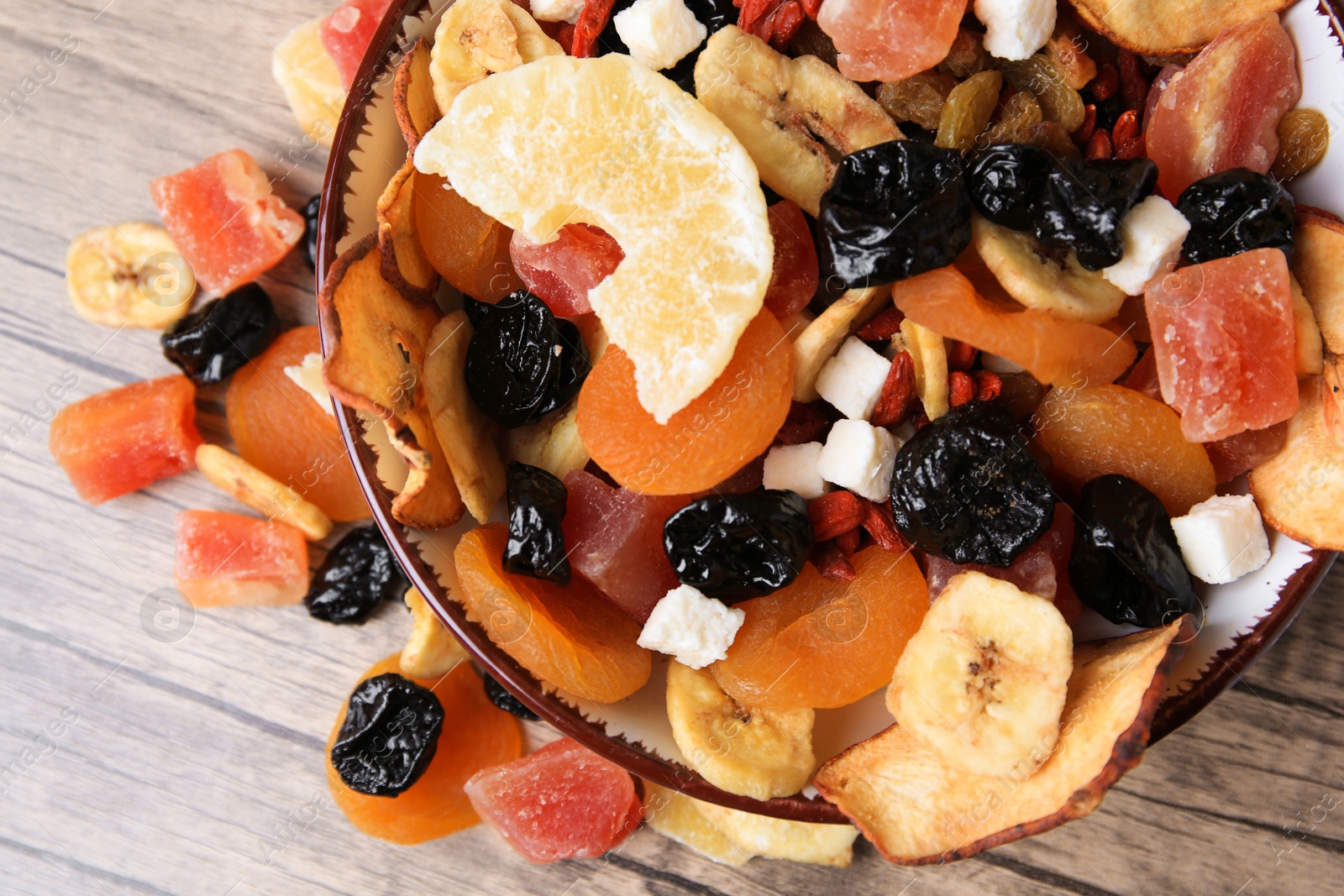 Photo of Bowl and different tasty dried fruits on wooden table, flat lay