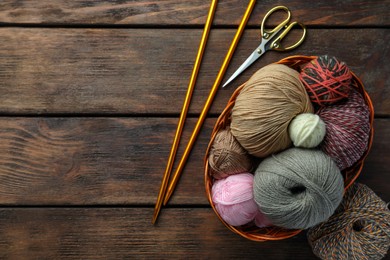 Photo of Soft woolen yarns, knitting needles and scissors on wooden table, flat lay. Space for text
