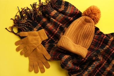 Photo of Stylish gloves, scarf and hat on yellow background, flat lay