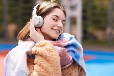 Photo of Beautiful woman in warm scarf listening to music outdoors
