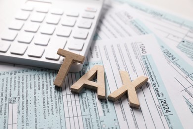 Word Tax made with wooden letters, calculator and documents on table, closeup