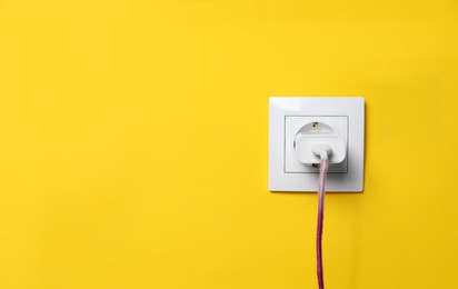 Charger adapter plugged into power socket on yellow wall, space for text. Electrical supply