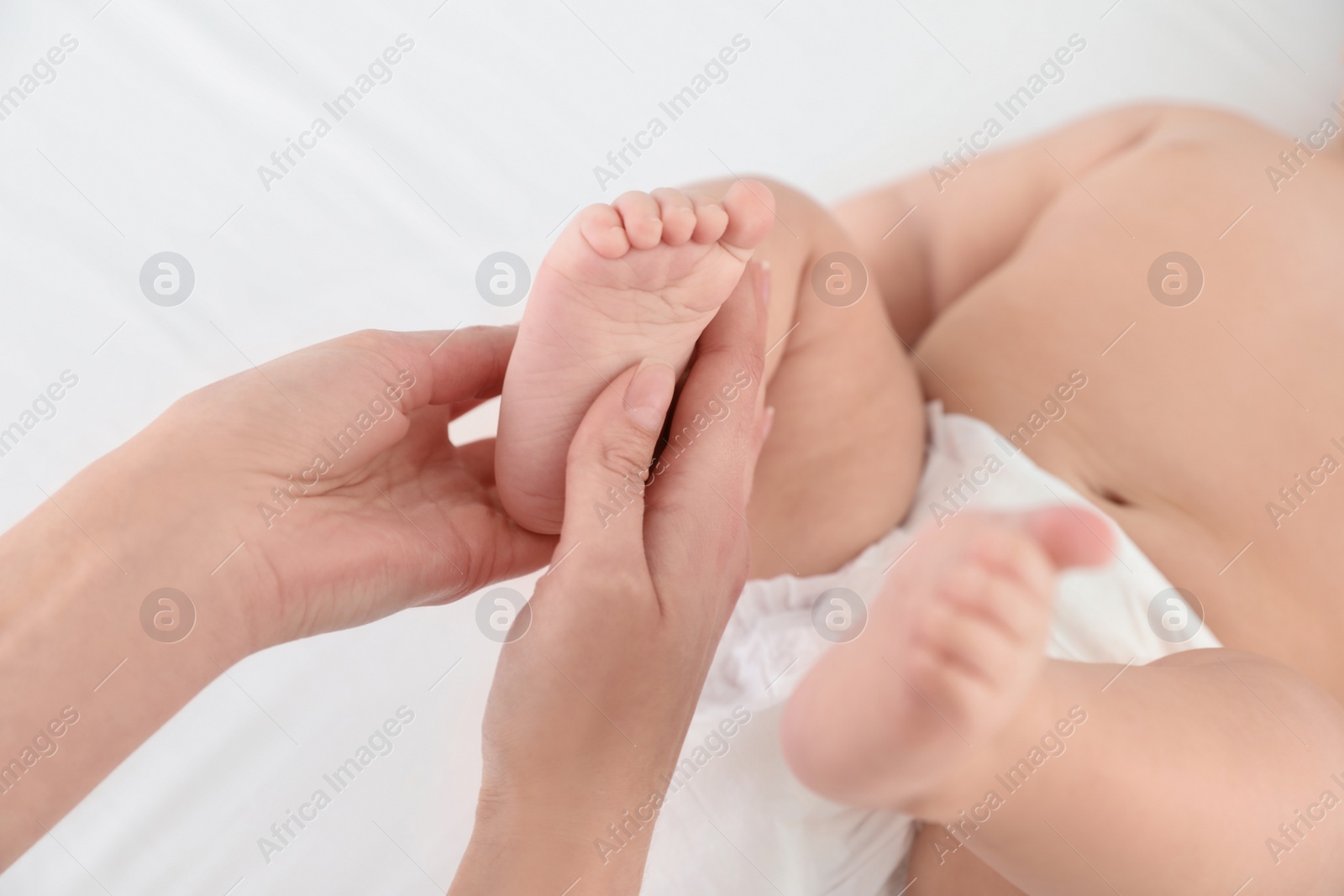 Photo of Mother and her cute child on white bed, closeup. Baby massage and exercises