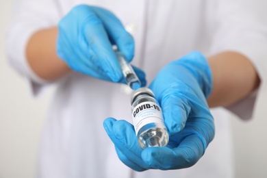 Doctor filling syringe with vaccine against Covid-19 on white background, closeup