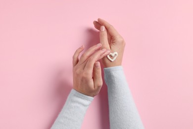 Photo of Woman with heart made of cosmetic cream on hand against pink background, top view