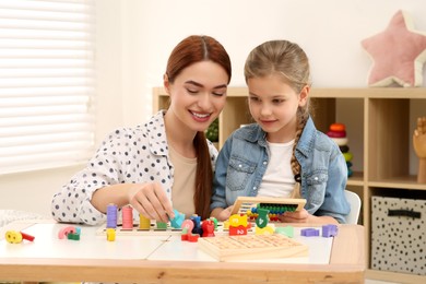 Happy mother and daughter playing with different math game kits at desk in room. Study mathematics with pleasure