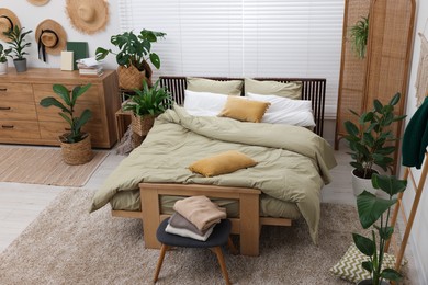 Photo of Stylish bedroom with comfortable bed and beautiful green houseplants. Interior design