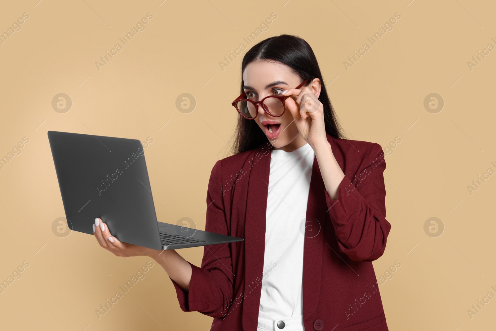 Photo of Shocked woman with laptop on beige background