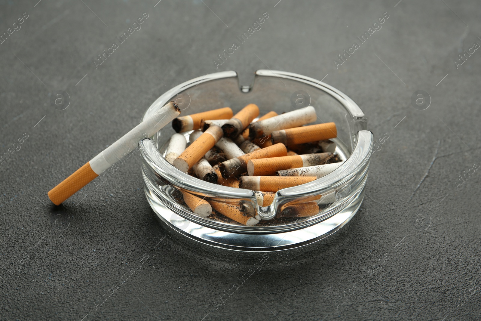 Photo of Glass ashtray full of cigarette stubs on grey table