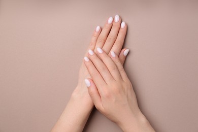 Photo of Woman showing her manicured hands with white nail polish on light brown background, top view