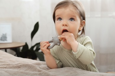 Photo of Cute baby girl with nibbler near bed at home