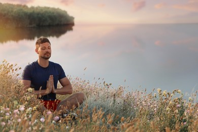 Photo of Man meditating in meadow near river. Space for text