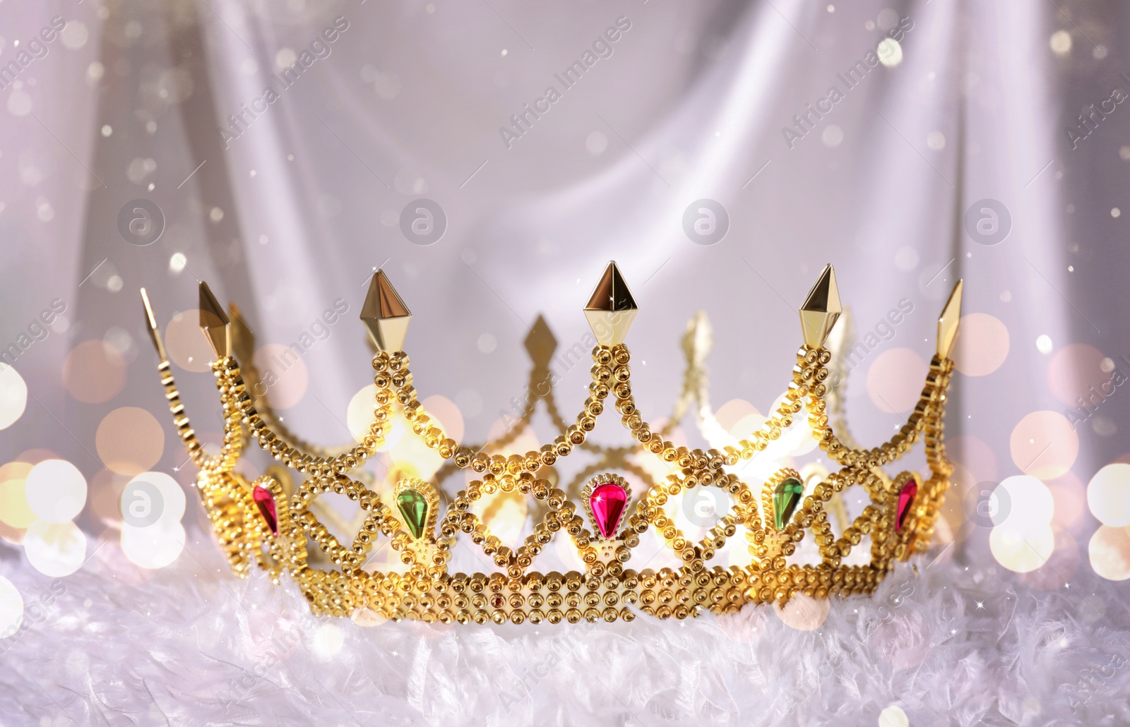 Image of Beautiful golden crown with gems on white fluffy cloth, bokeh effect