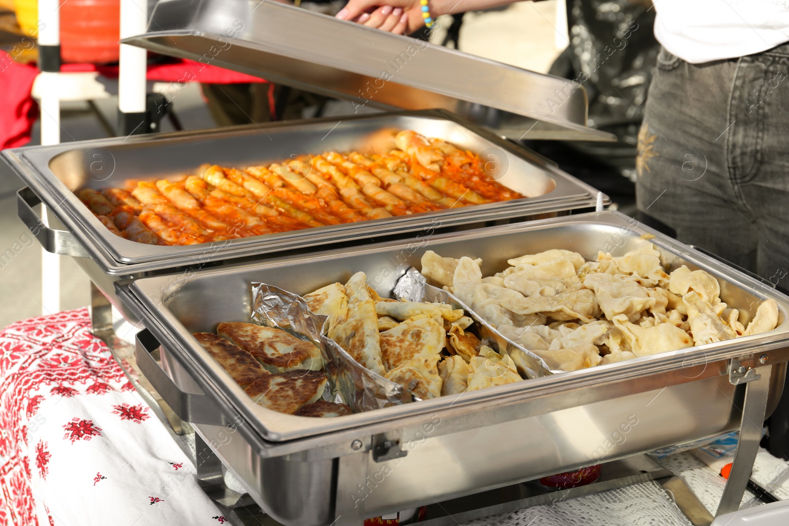 Photo of Female volunteer distributing delicious stuffed cabbage, dumplings and patties from food warmers