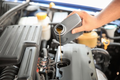 Photo of Mechanic pouring oil into car engine, closeup