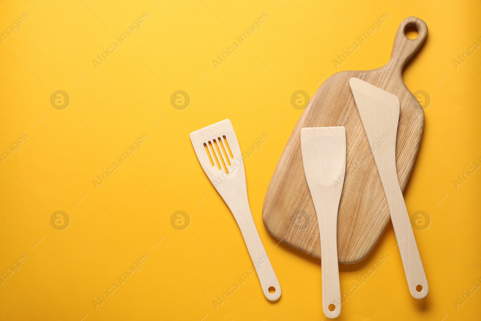 Photo of Different wooden spatulas and board on orange background, flat lay. Space for text