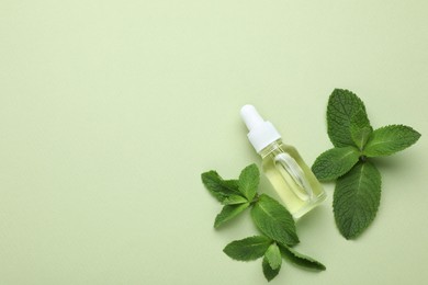Photo of Bottle of essential oil and mint on light green background, flat lay. Space for text