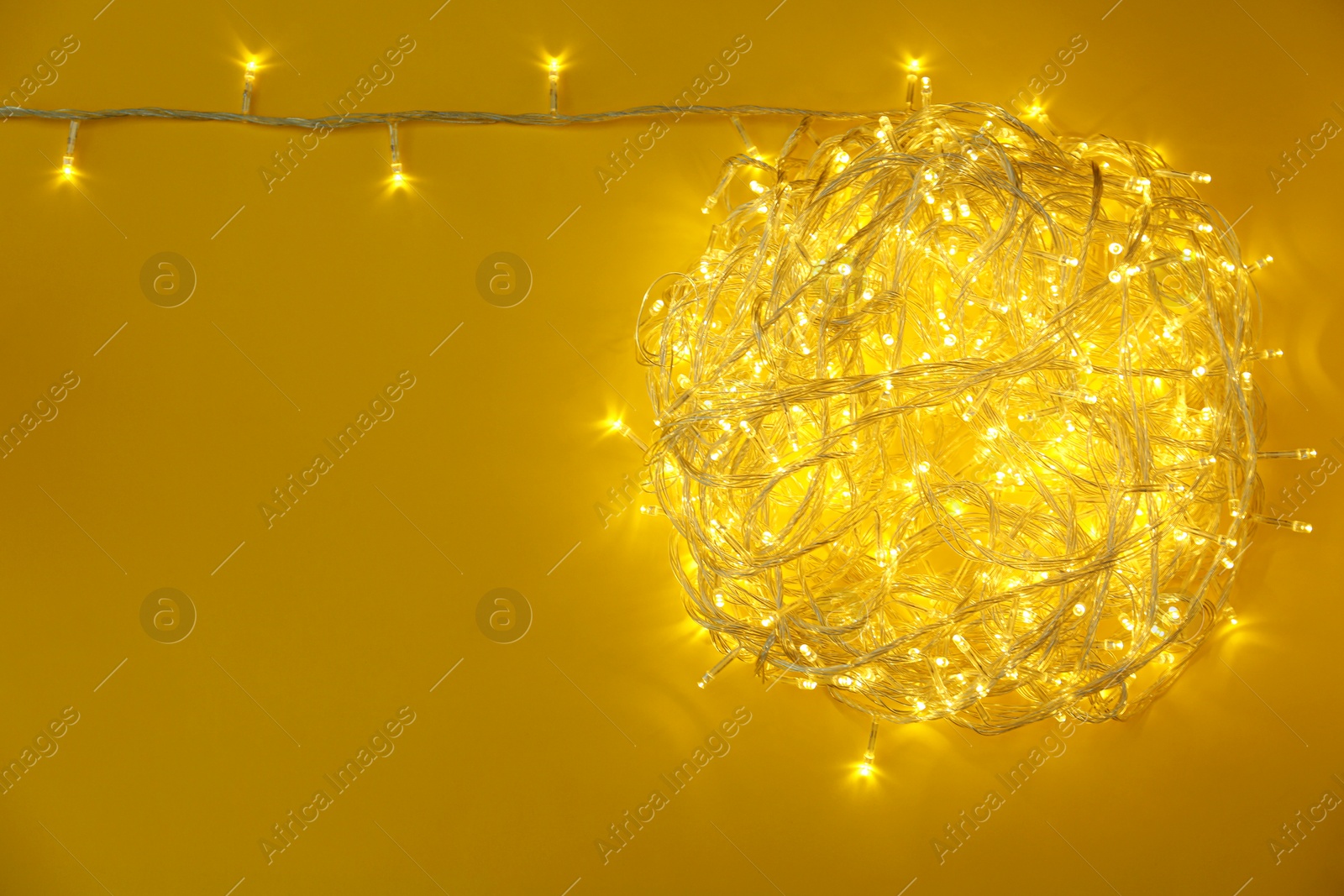 Photo of Glowing Christmas lights on yellow background, top view. Space for text