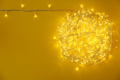 Photo of Glowing Christmas lights on yellow background, top view. Space for text