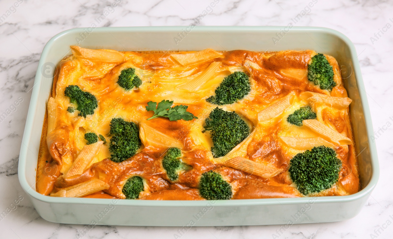 Photo of Tasty broccoli casserole in baking dish on white marble table, closeup