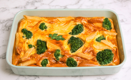 Photo of Tasty broccoli casserole in baking dish on white marble table, closeup