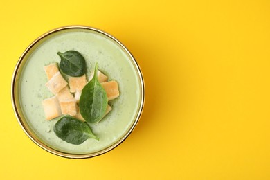 Photo of Delicious spinach cream soup with croutons in bowl on yellow background, top view. Space for text