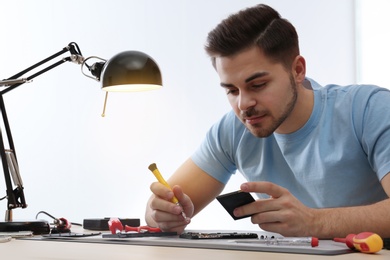 Photo of Technician repairing broken smartphone at table in workshop