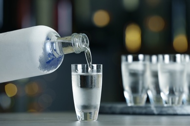 Pouring vodka from bottle into shot glass on bar counter