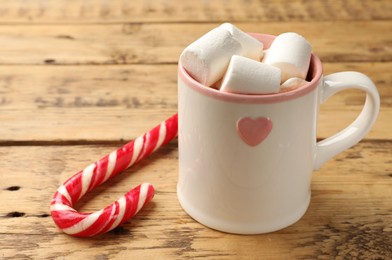 Photo of Tasty hot chocolate with marshmallows and candy cane on wooden table, closeup