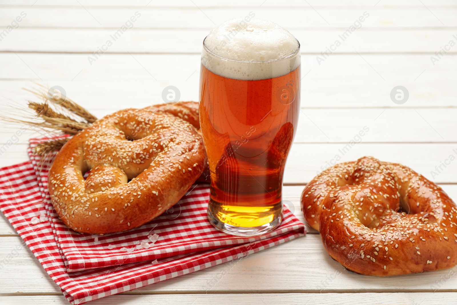 Photo of Glass of beer and tasty freshly baked pretzels on white wooden table
