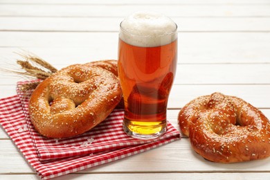 Glass of beer and tasty freshly baked pretzels on white wooden table