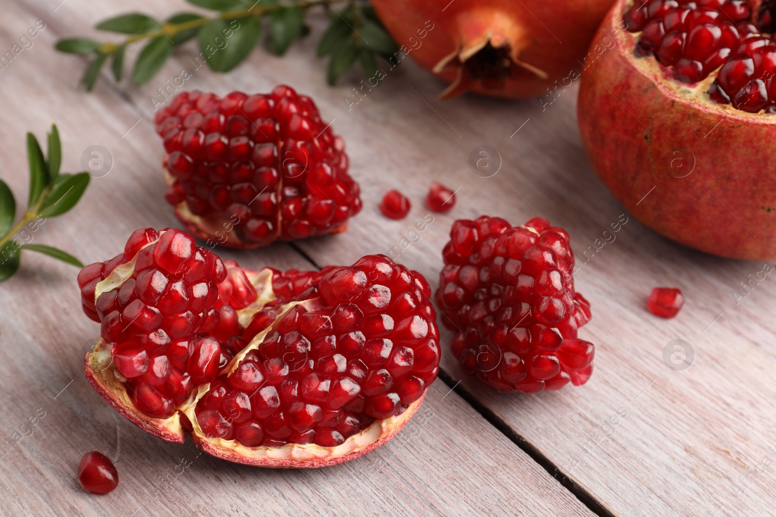 Photo of Cut fresh pomegranate and green leaves on wooden table, closeup