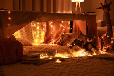 Photo of Beautiful play tent decorated with festive lights and toys at home