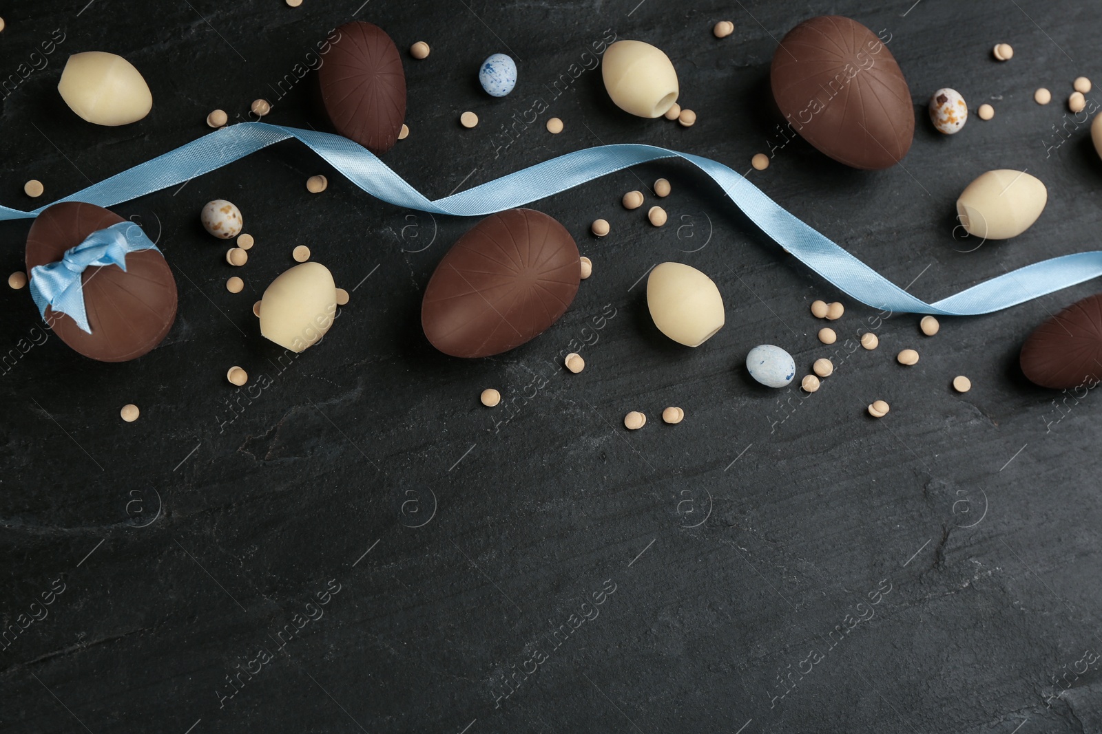 Photo of Sweet chocolate eggs and candies on black table, flat lay. Space for text