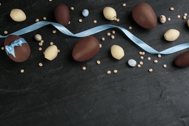 Sweet chocolate eggs and candies on black table, flat lay. Space for text