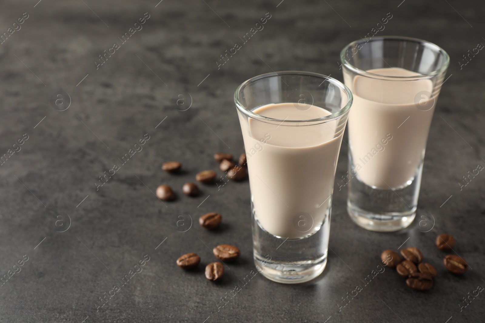 Photo of Coffee cream liqueur in glasses and beans on grey table, closeup. Space for text