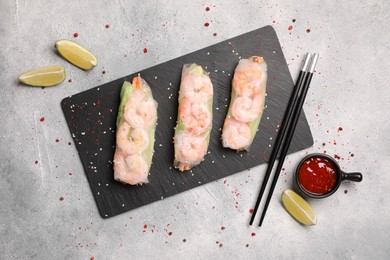 Photo of Tasty spring rolls served with spices, lime and sauce on grey textured table, flat lay