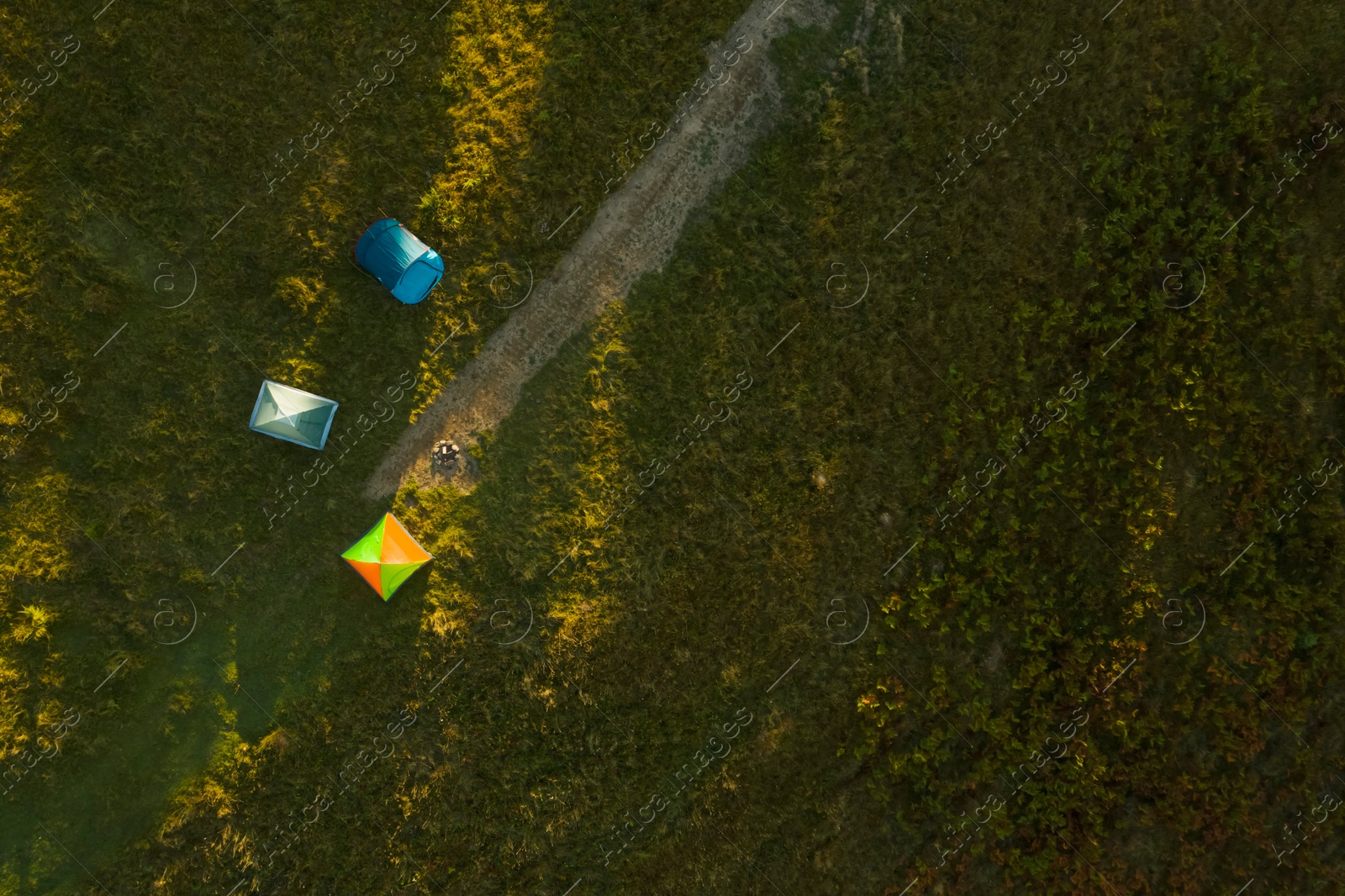 Image of Aerial view of camping tents and bonfire on green meadow