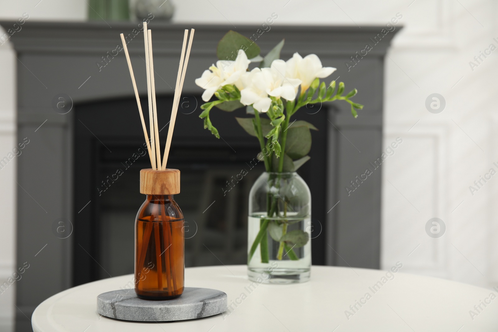 Photo of Reed diffuser and vase with bouquet on white table in room