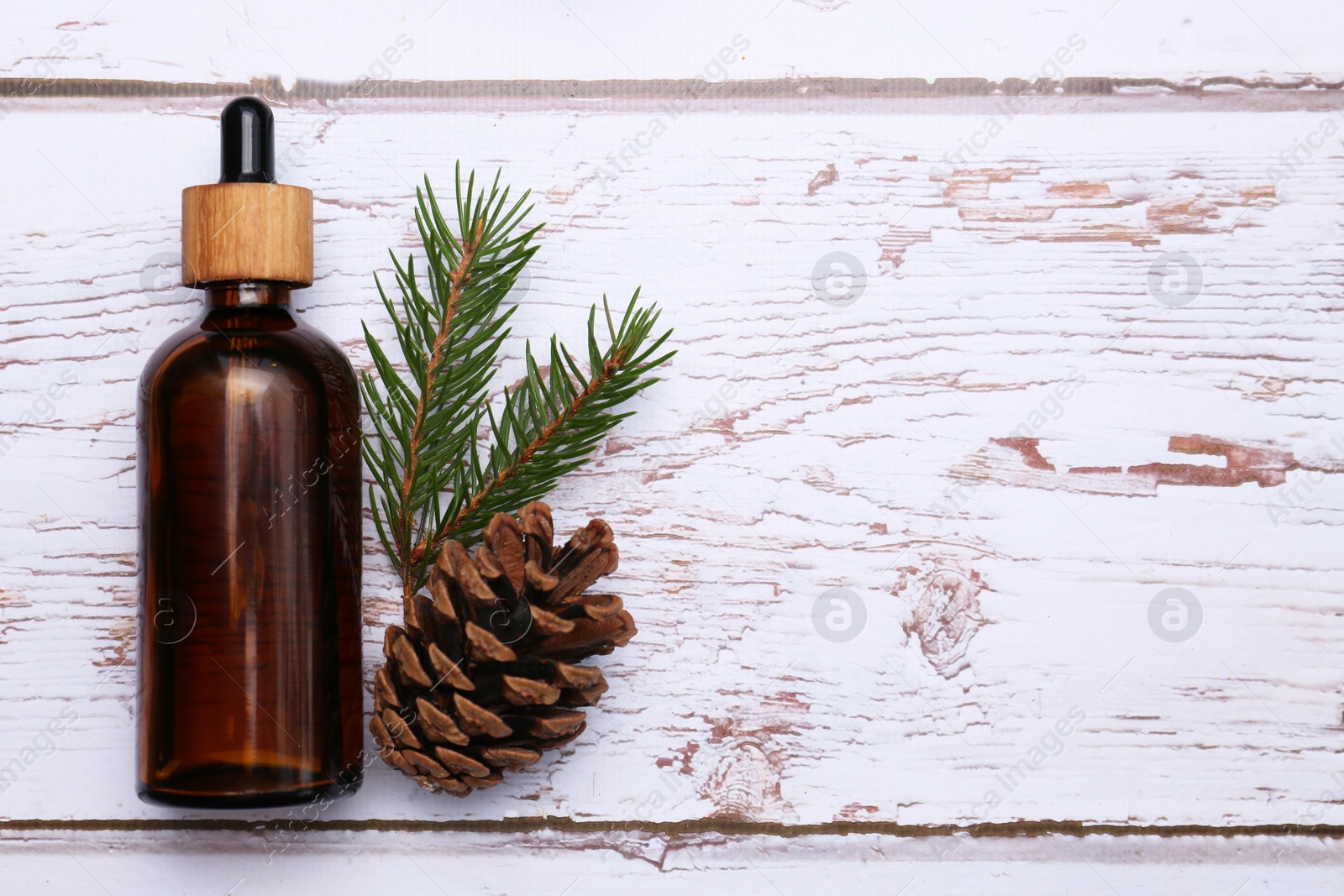 Photo of Bottle of pine essential oil, conifer tree branch and cone on white wooden table, top view. Space for text