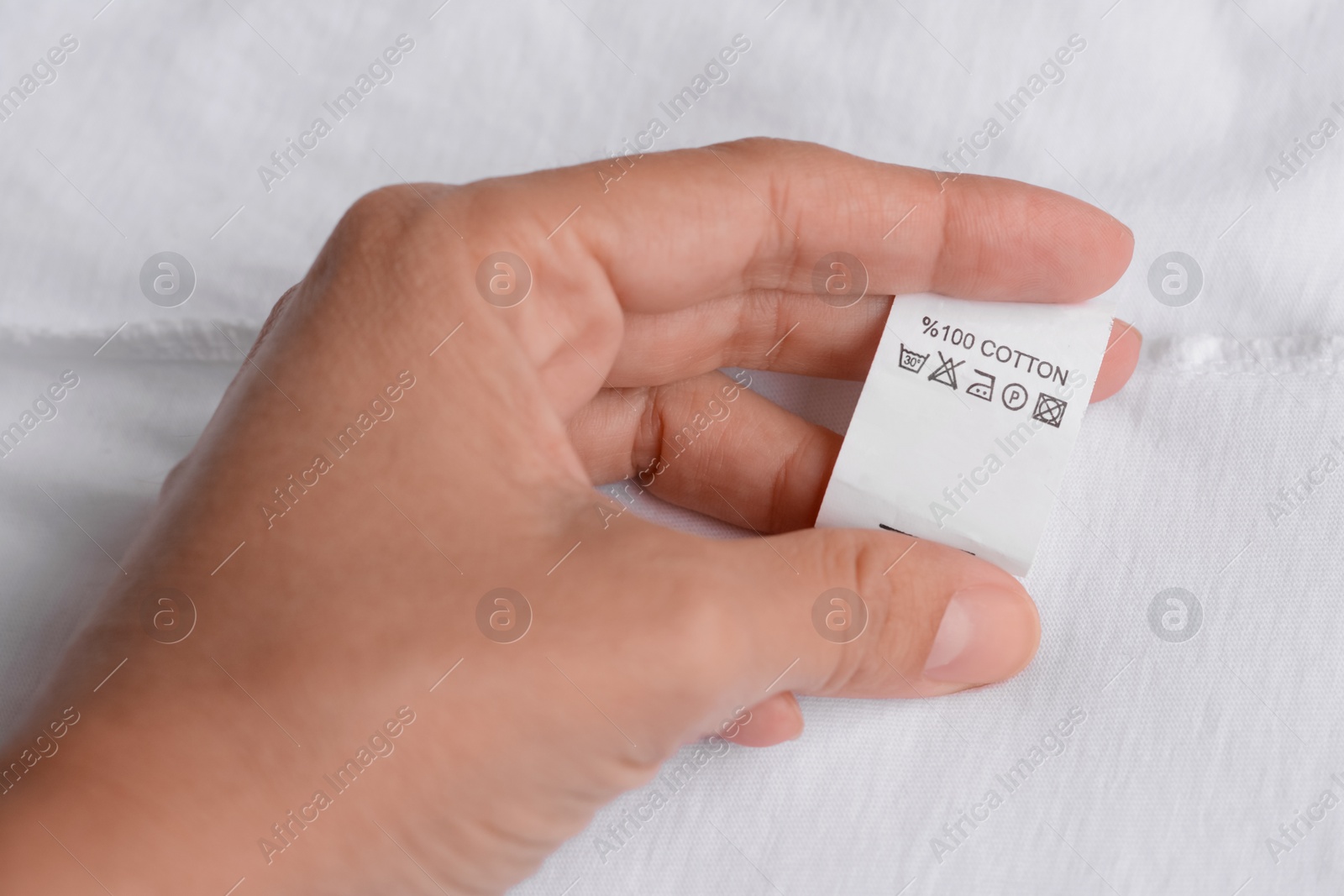 Photo of Woman holding clothing label on white garment, closeup